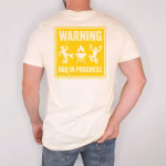 Man standing wearing a Warning BBQ In Progress Shirt in the sand color variant.